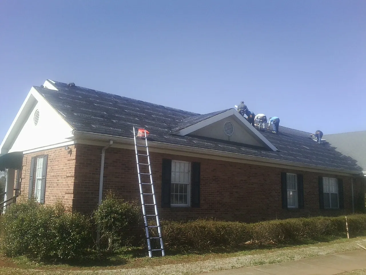 Crew tearing shingles off a brick ranch roof with a ladder set — Emergency Roof Repair work by our crew in Seaford