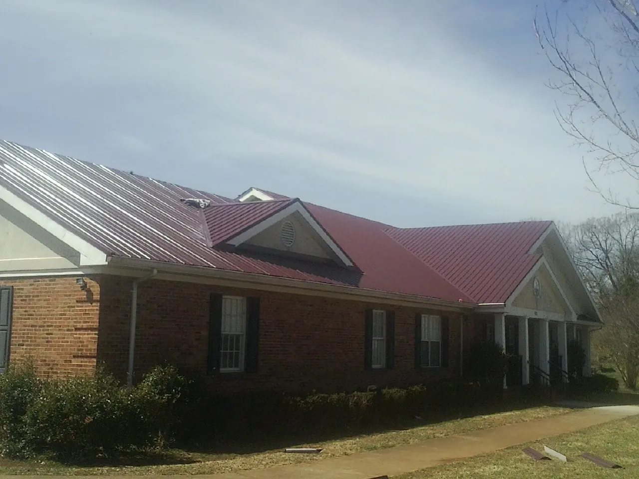 Red metal roof with gabled entries on a long brick building, from a Hail Damage Roof Repair job in Seaford